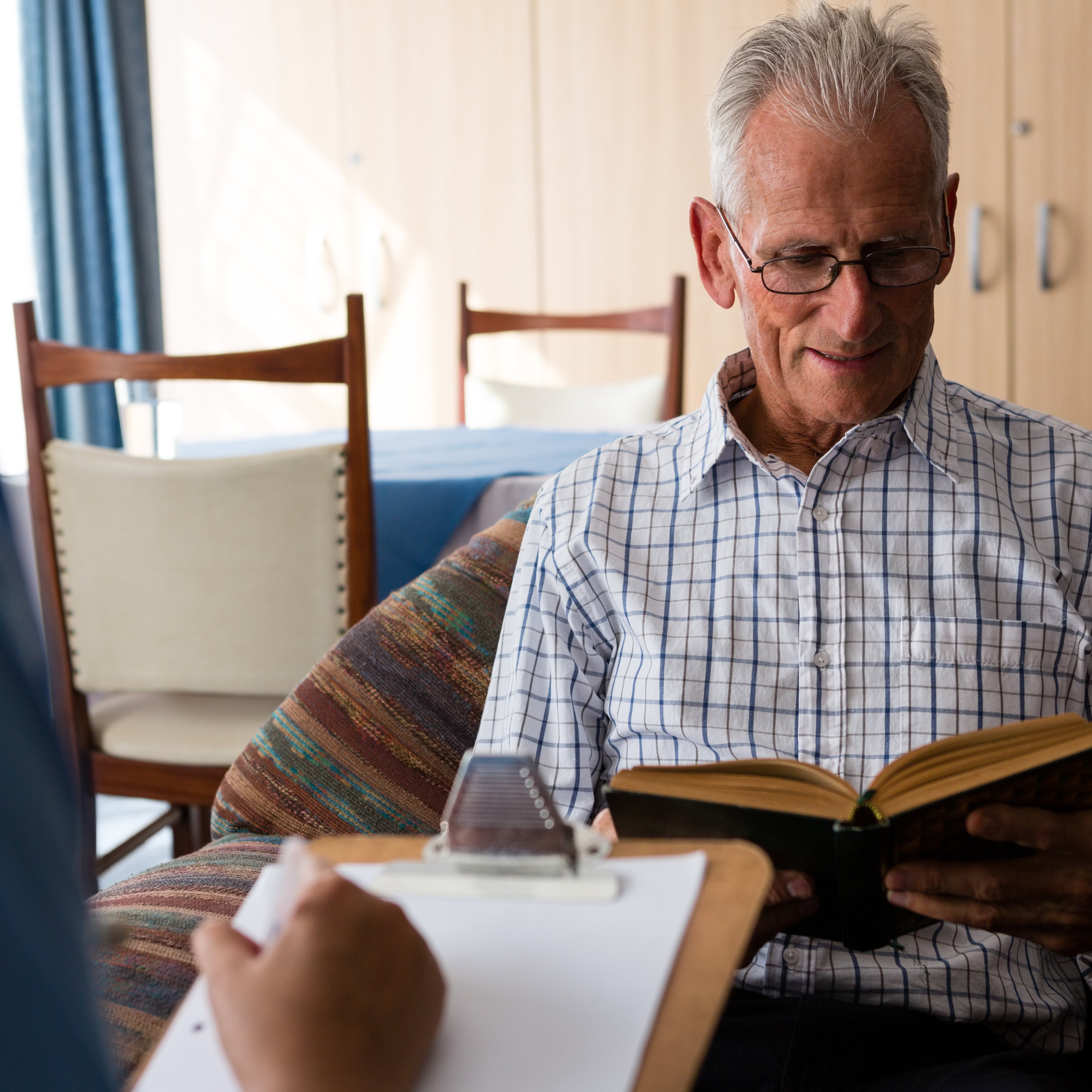 Female doctor writing on paper while senior man reading book in nursing home