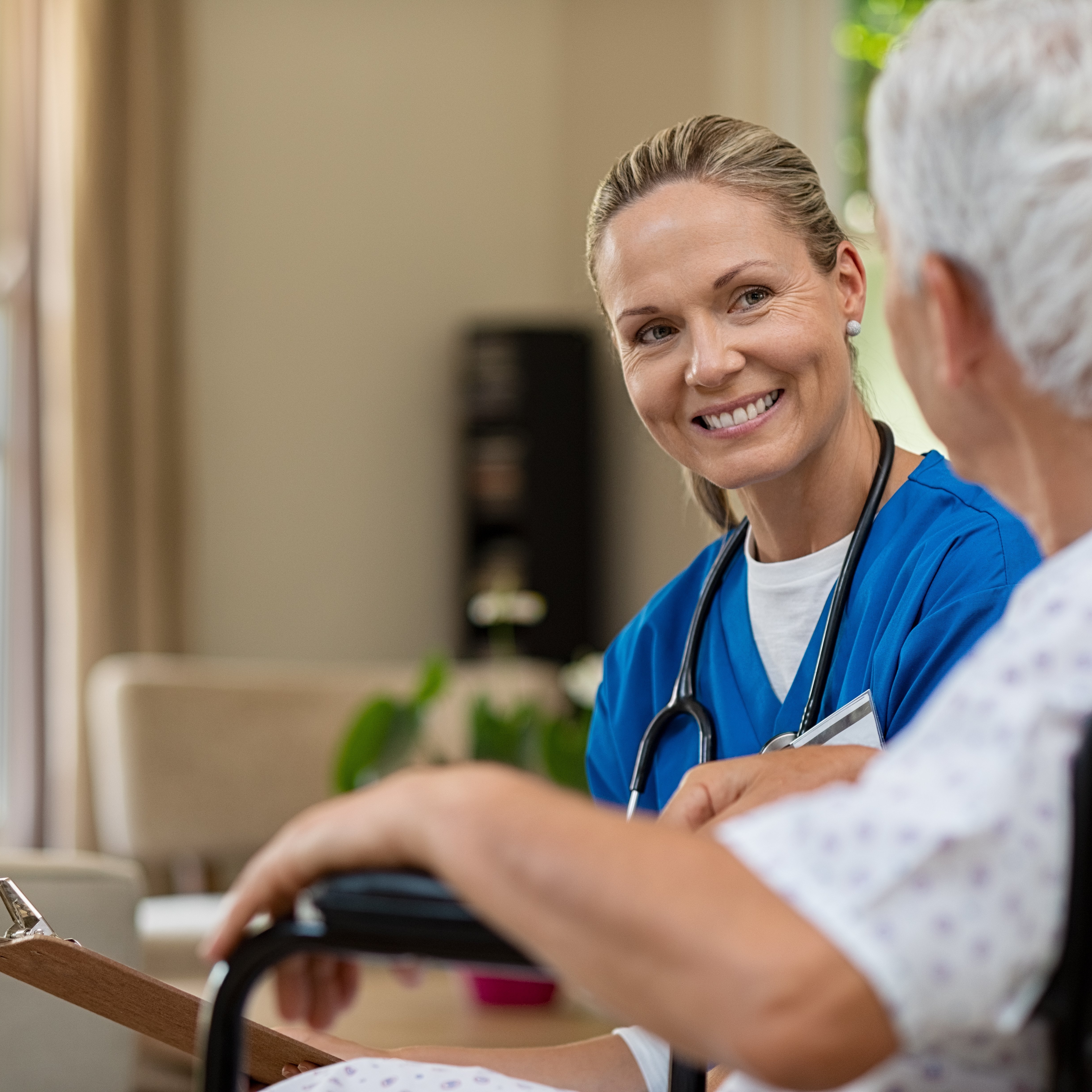 Friendly doctor examining health of patient sitting in wheelchair. Happy smiling nurse consulting disabled patient about treatment. Nurse caring about elder handicap man at home.